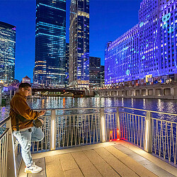 A person standing before a digital art projection at Art on the Mart on the Chicago River at night.