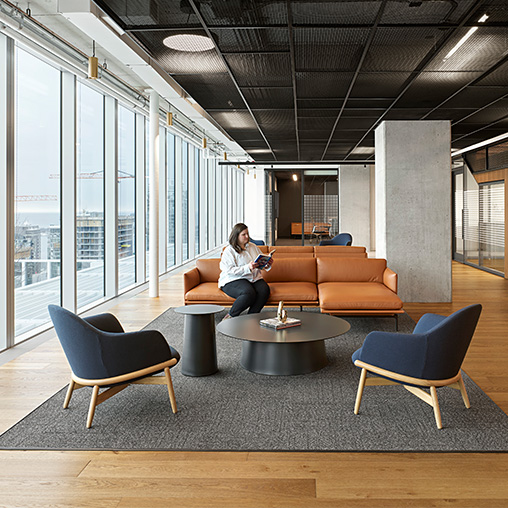 A person sitting on a couch in an office lounge room with a table and chairs.