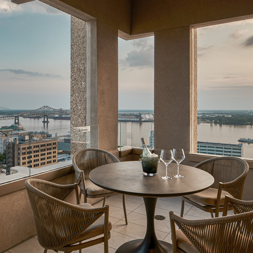 A table with chairs and glasses on it by a window with a view of the water and buildings.