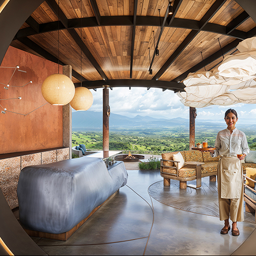 A person standing in a room with a large bed and a view of the mountains.