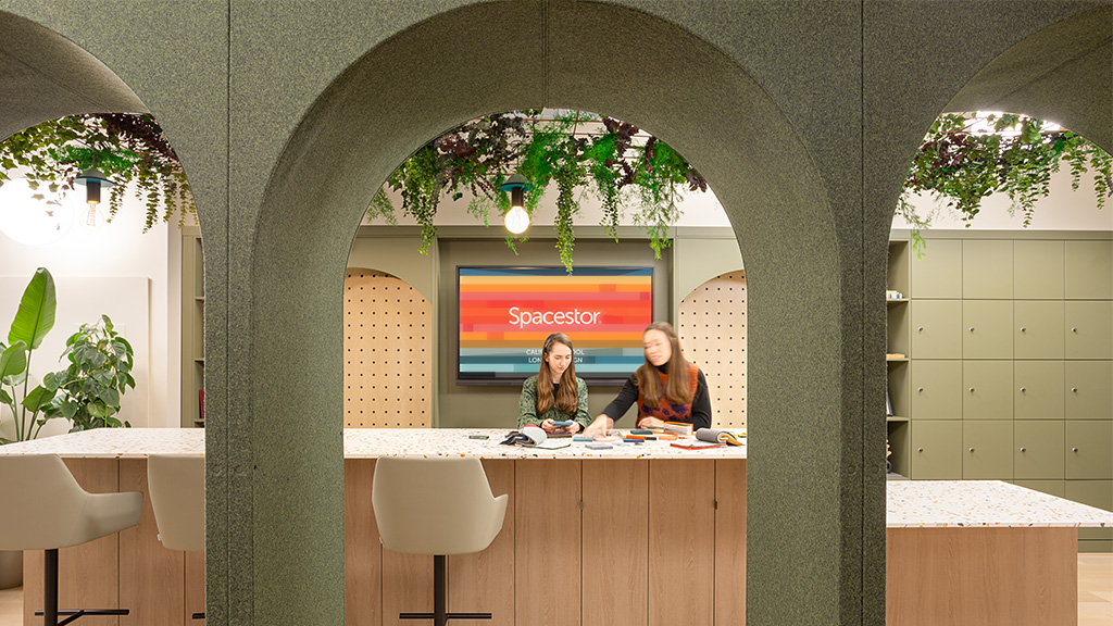 A couple of women sitting at a table in a room with a large screen.