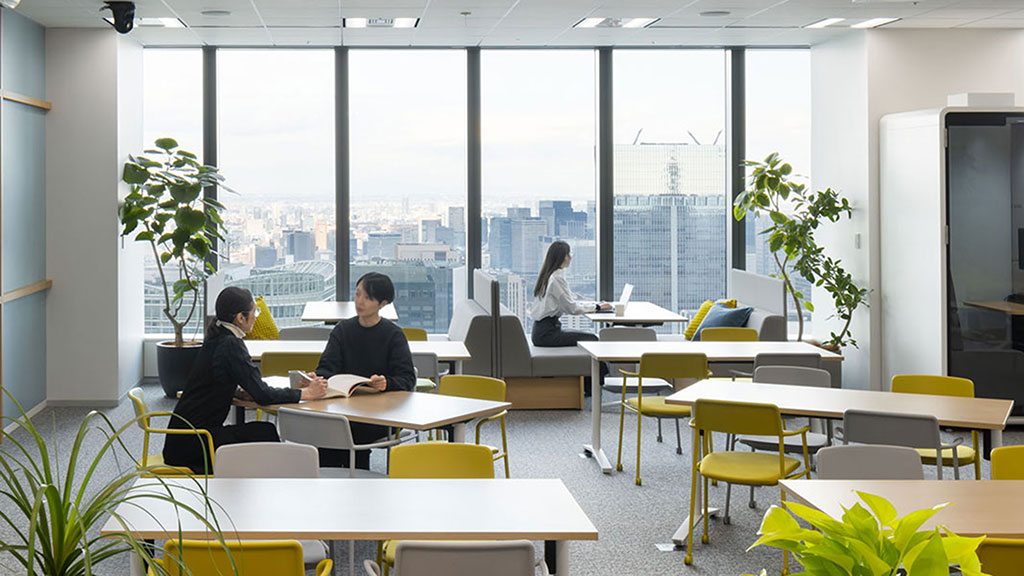 A group of people sitting at tables in a room with large windows.